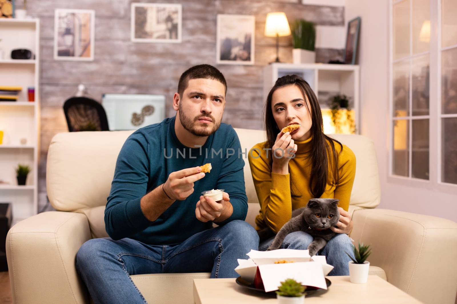 Young couple eating fried chicken in front of the TV by DCStudio