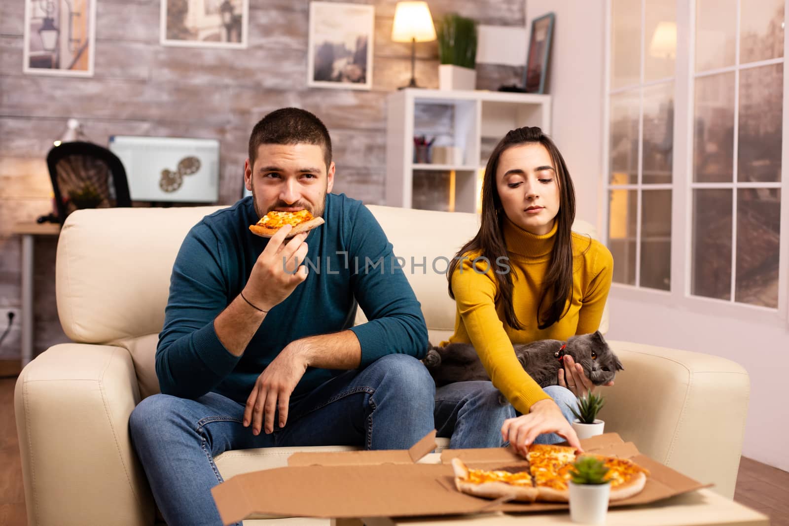 Gorgeous young couple eating pizza while watching TV in the living room sitting on the sofa