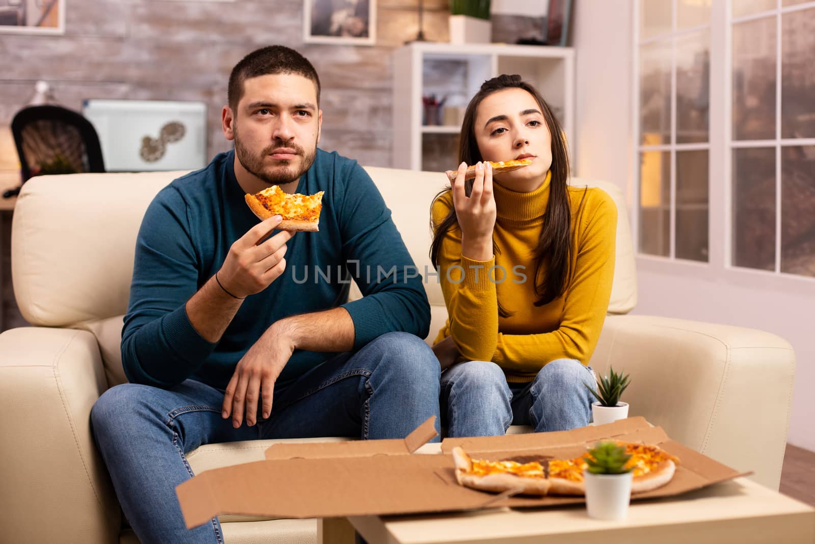 Gorgeous young couple eating pizza while watching TV in the living room sitting on the sofa