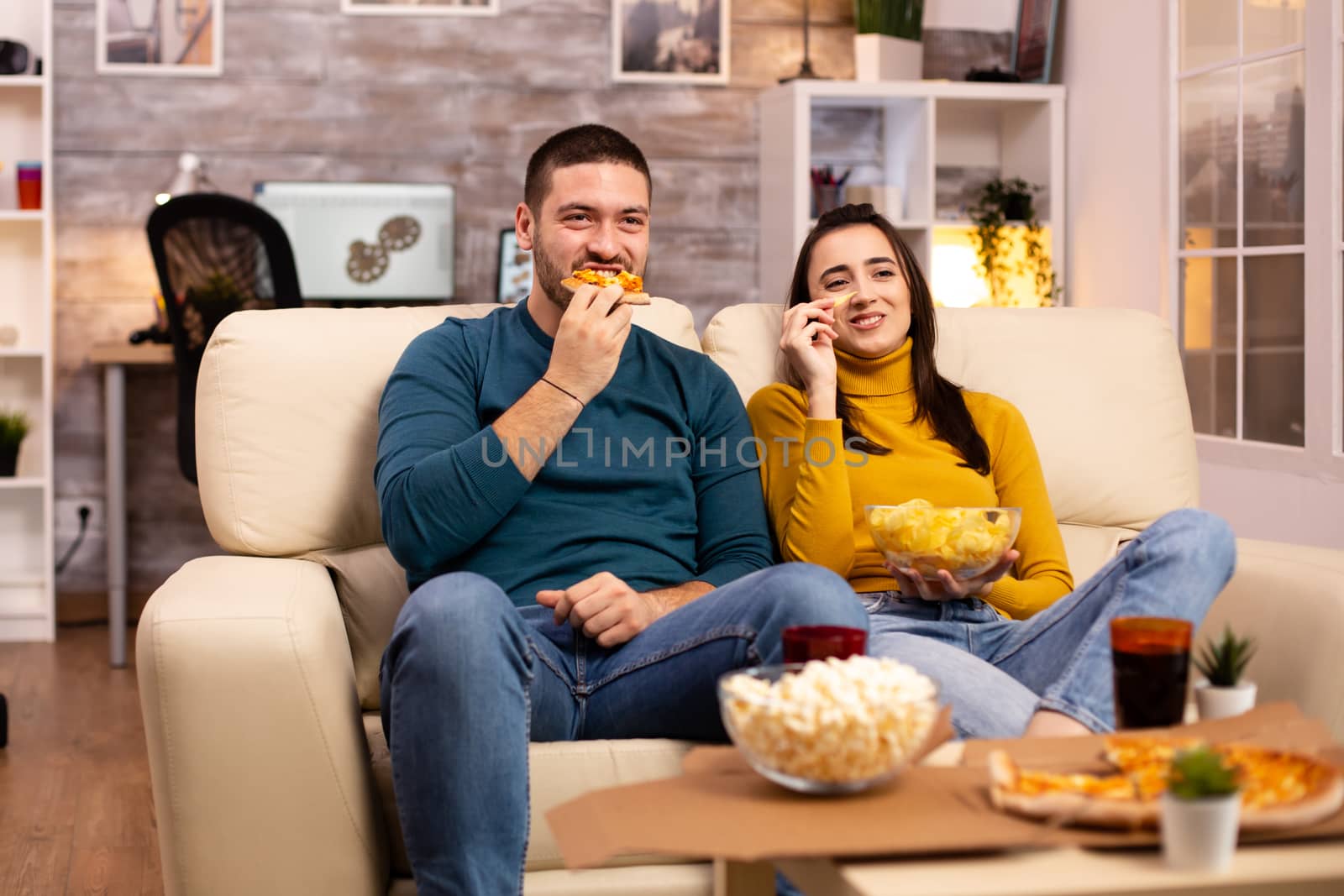 Beautiful young couple watching TV and eating fast food takeaway by DCStudio