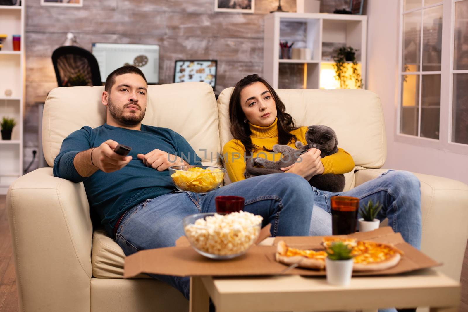 Beautiful young couple watching TV and eating fast food takeaway in the living room