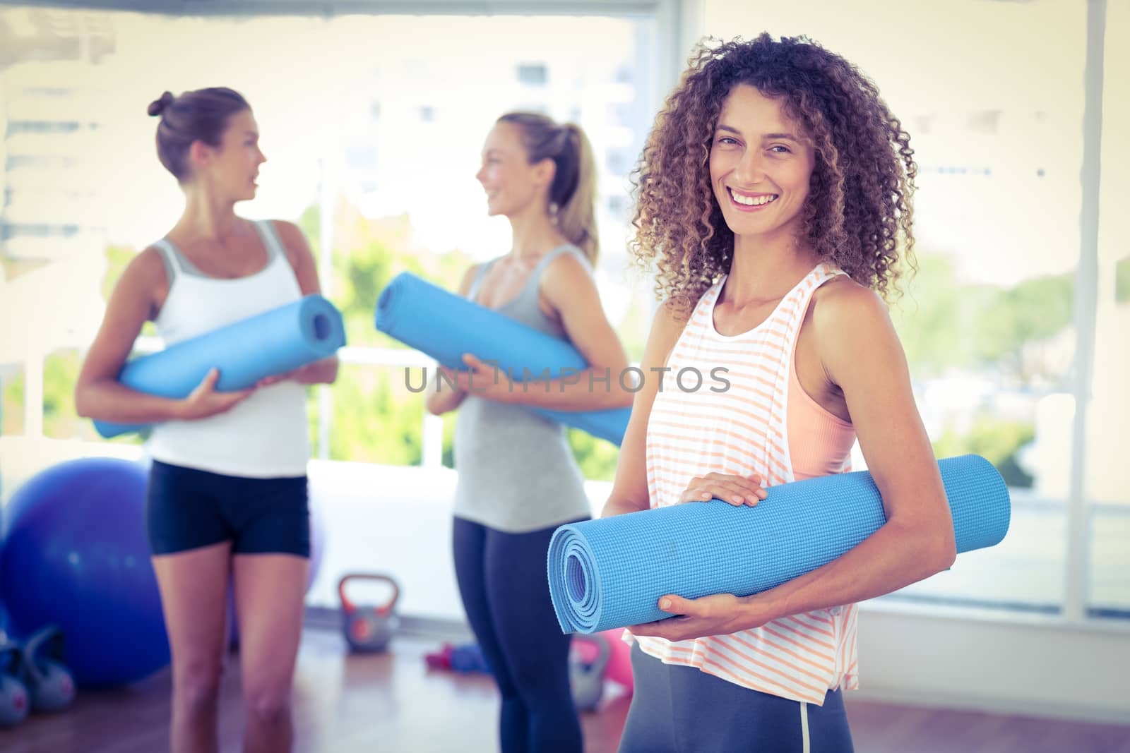 Portrait of woman holding yoga mat and smiling in fitness studio