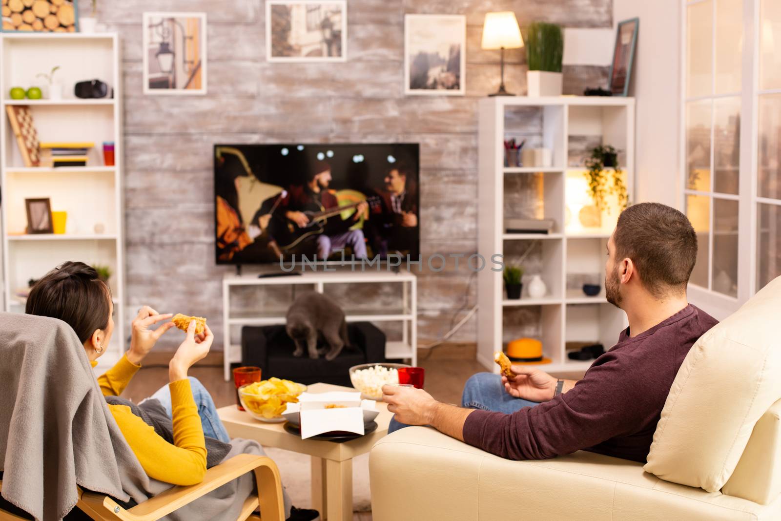 Back view of couple in living room watching a movie on the TV by DCStudio