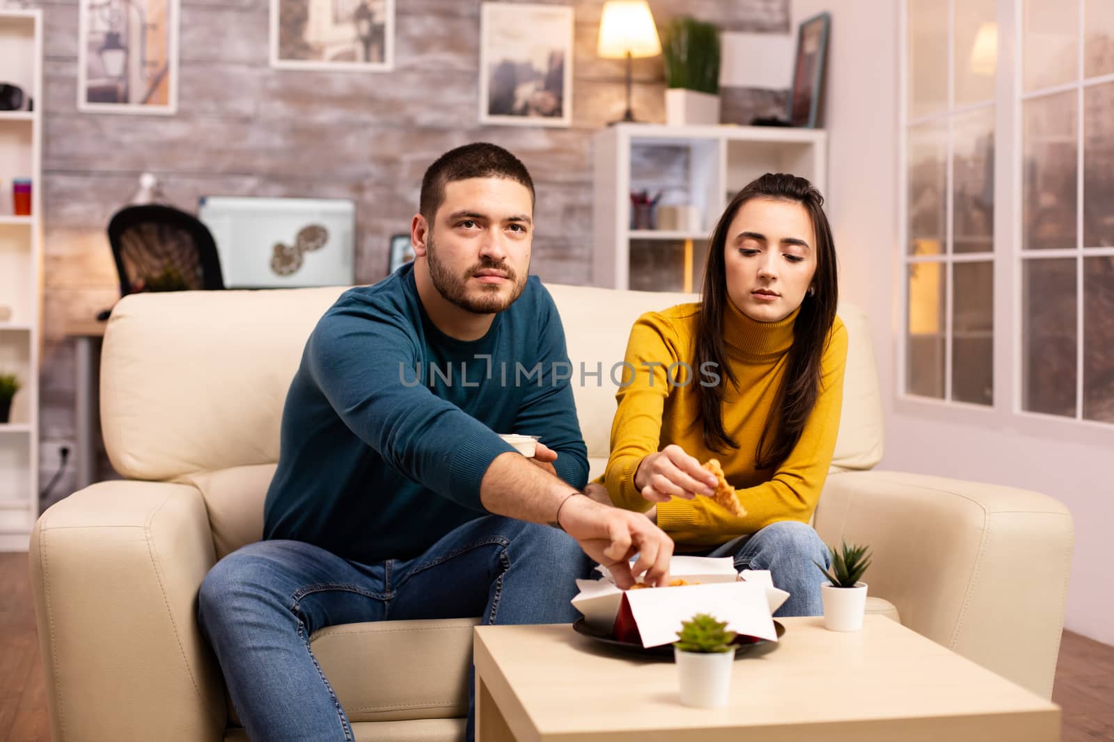 Young couple eating fried chicken in front of the TV in the living room