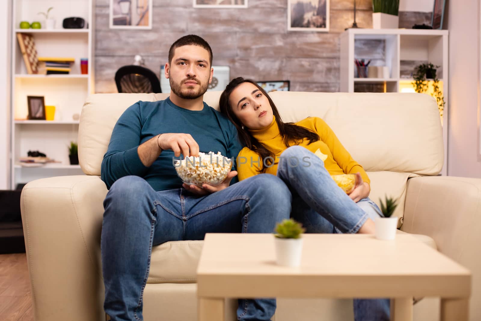 Handsome couple at home eating pop corn and watching TV on the sofa in the living room