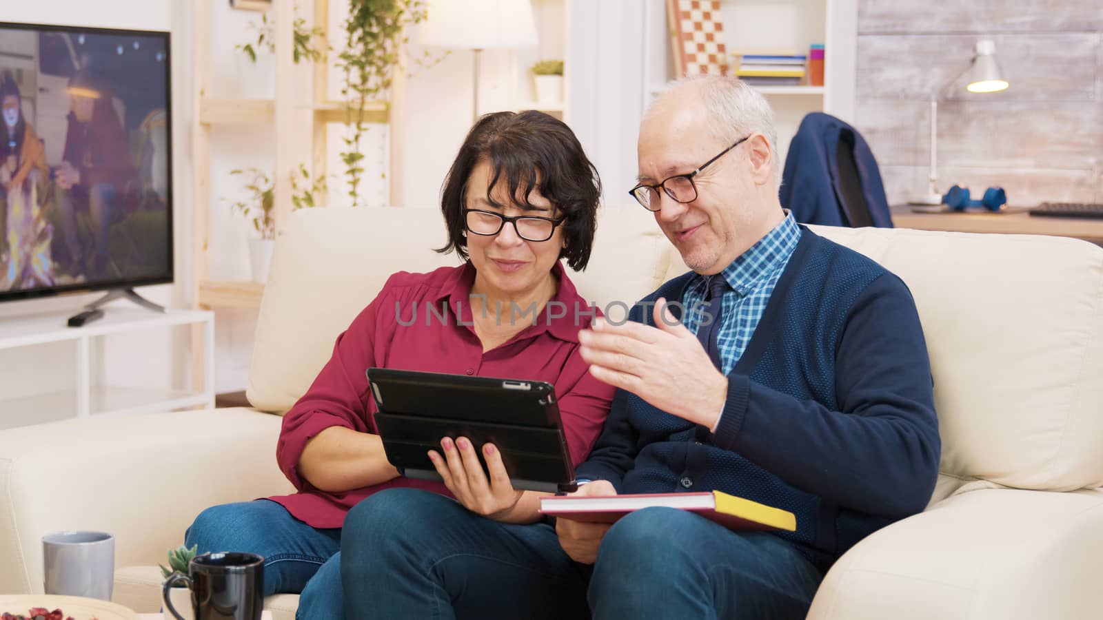 Old couple sitting on sofa during a video call on tablet by DCStudio