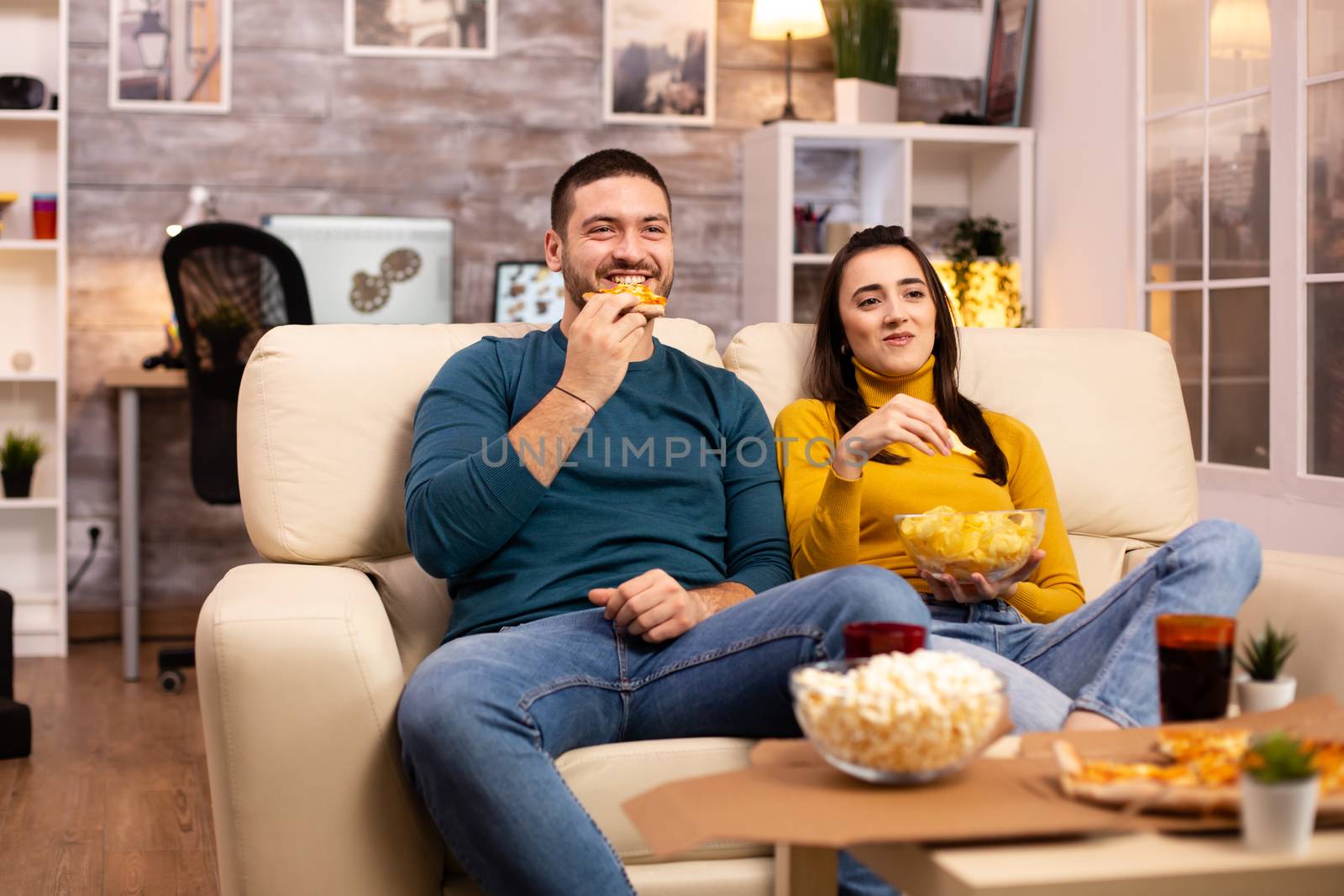 Beautiful young couple watching TV and eating fast food takeaway by DCStudio