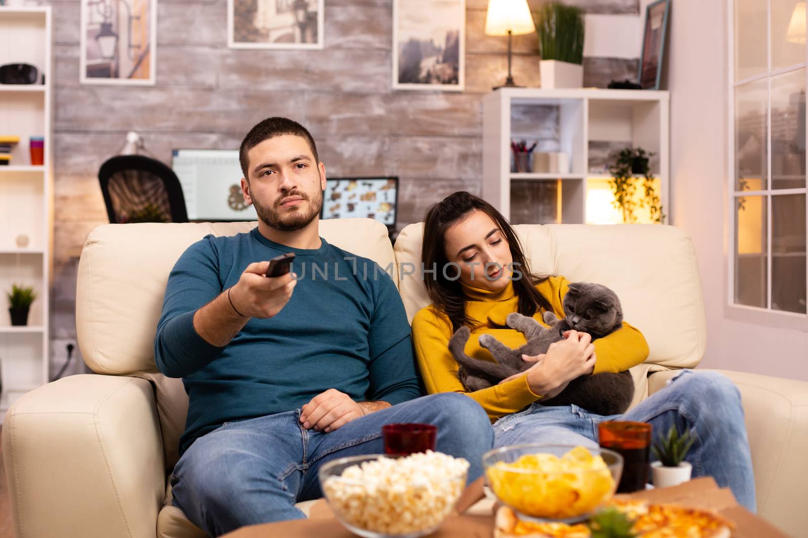 Beautiful young couple watching TV and eating fast food takeaway in the living room