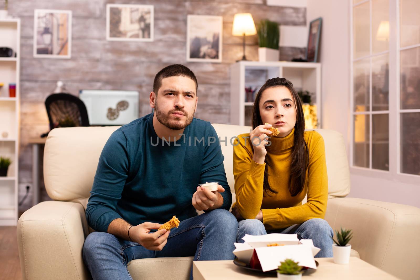 Young couple eating fried chicken in front of the TV by DCStudio