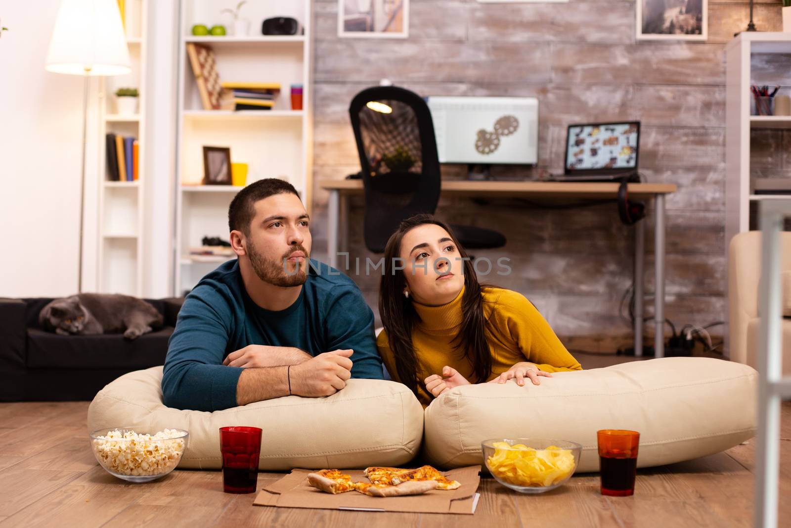 Couple sitting on the floor and watching TV in their living room.