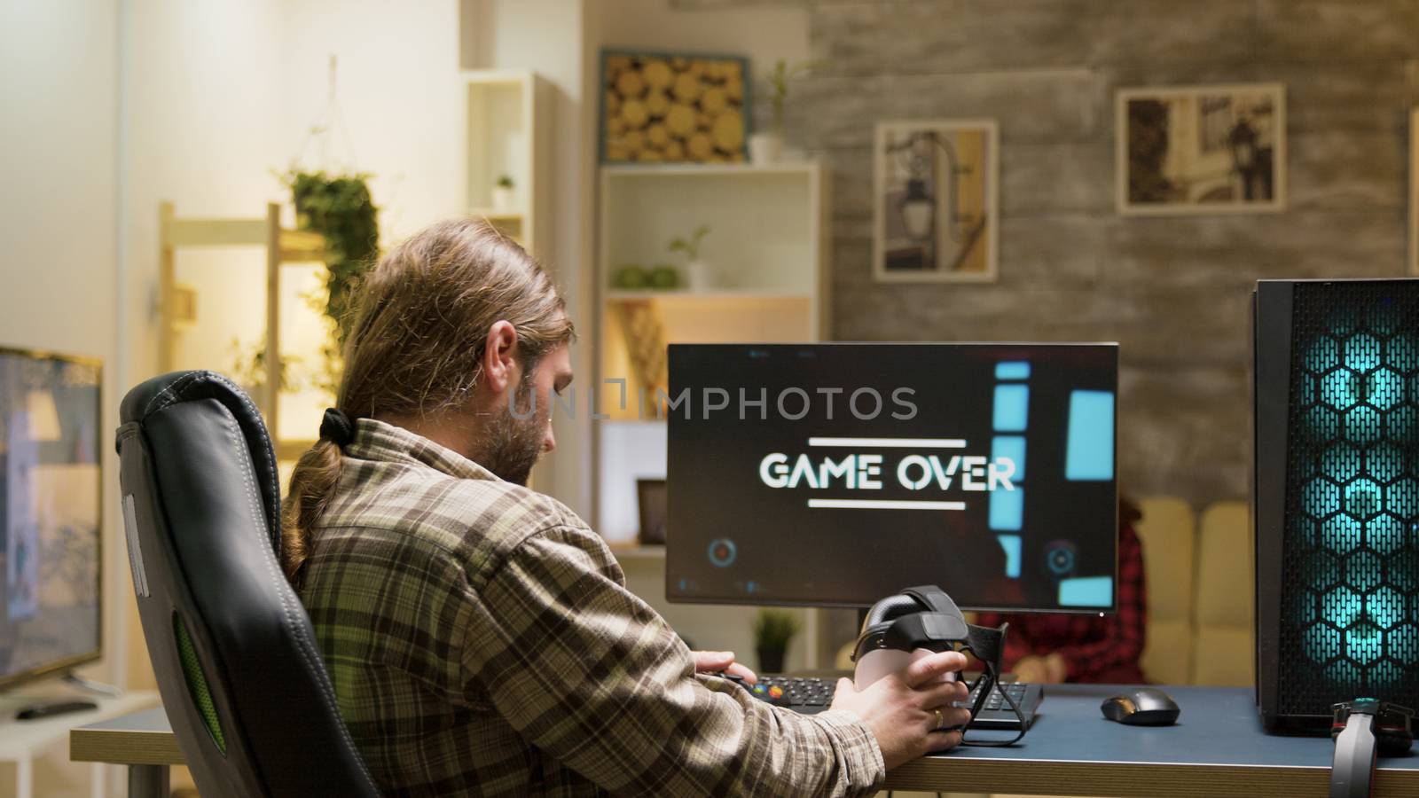 Game over for adult man playing video games using vr headset. Woman sitting on sofa watching tv in the background.