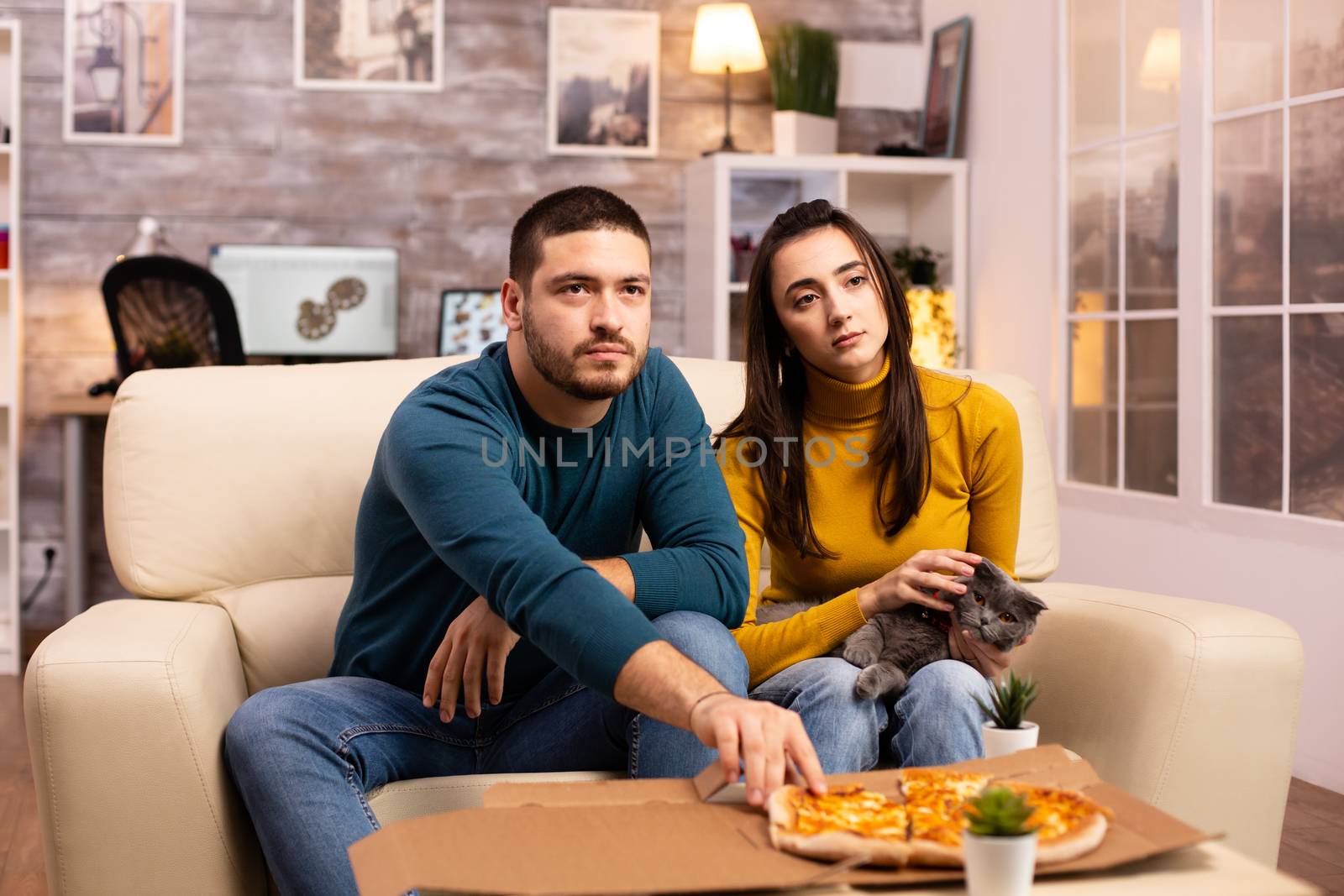 Gorgeous young couple eating pizza while watching TV by DCStudio