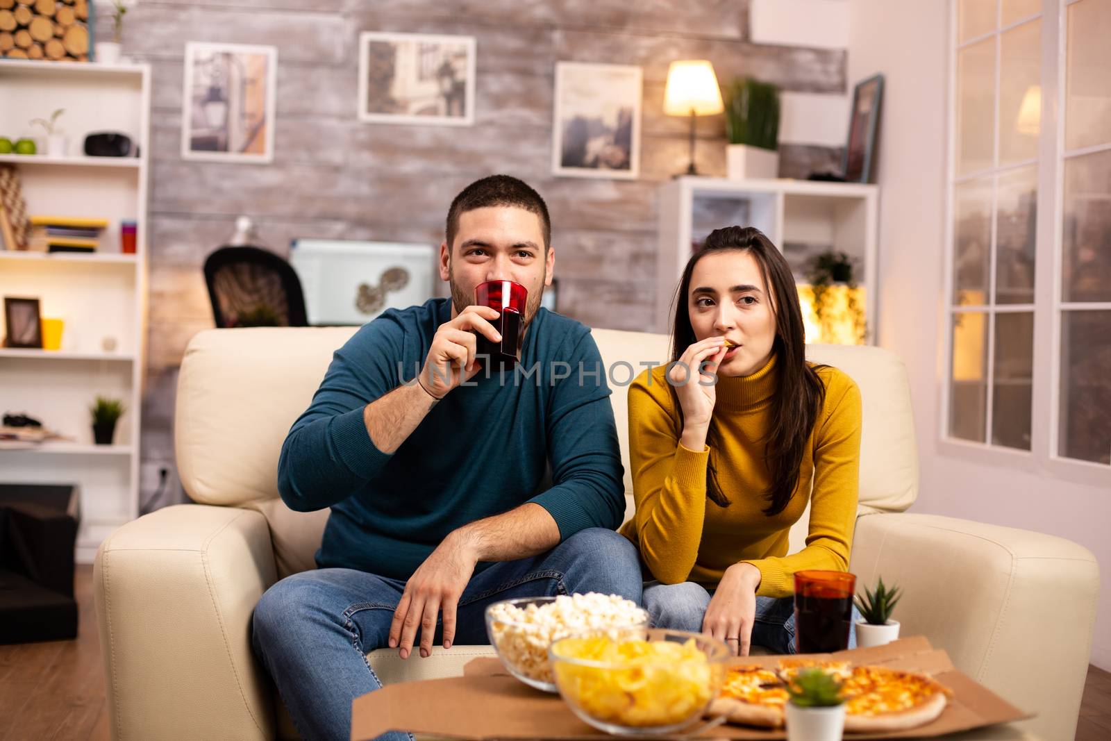 Beautiful young couple watching TV and eating fast food takeaway by DCStudio