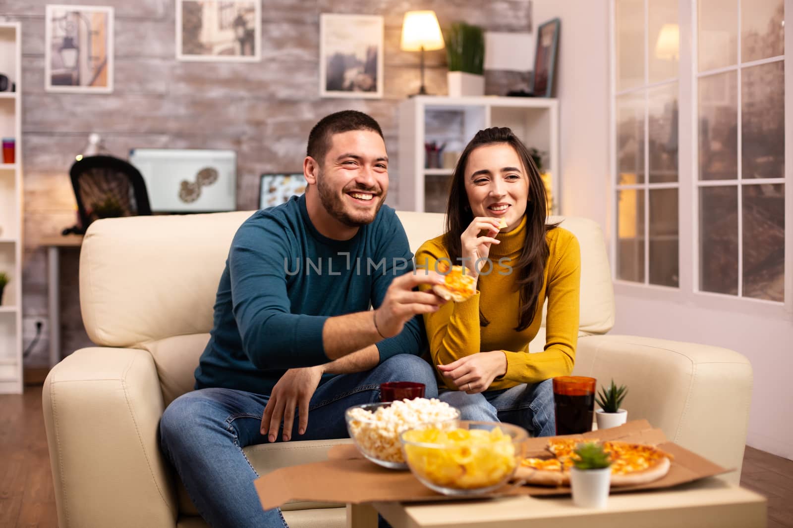 Beautiful young couple watching TV and eating fast food takeaway by DCStudio