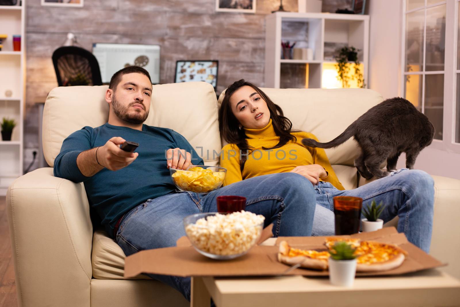 Beautiful young couple watching TV and eating fast food takeaway in the living room