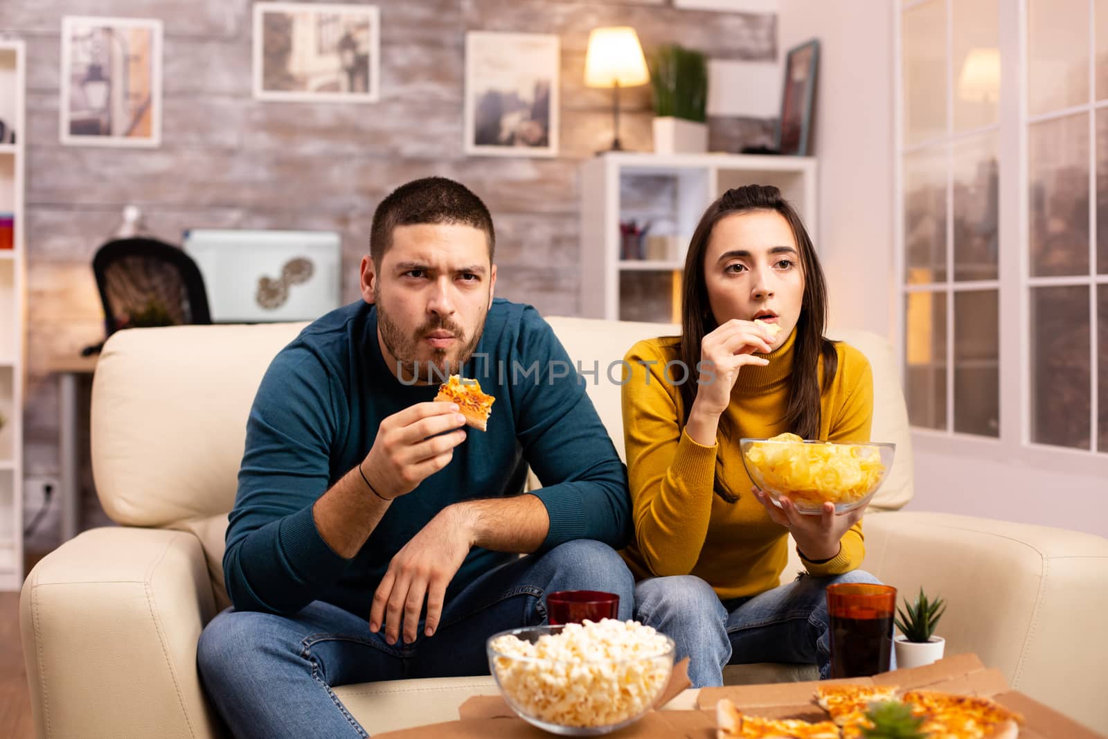 Beautiful young couple watching TV and eating fast food takeaway by DCStudio