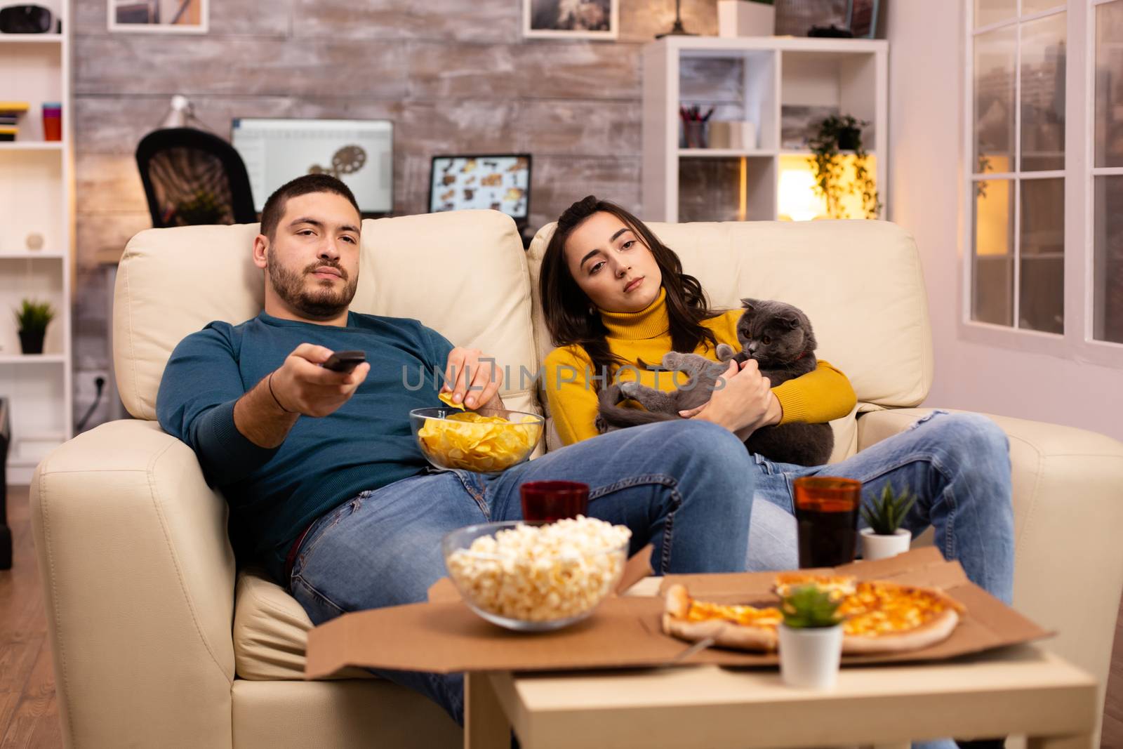 Beautiful young couple watching TV and eating fast food takeaway in the living room