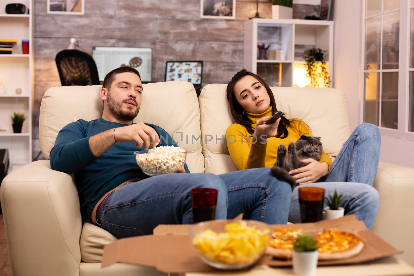 Beautiful young couple watching TV and eating fast food takeaway by DCStudio