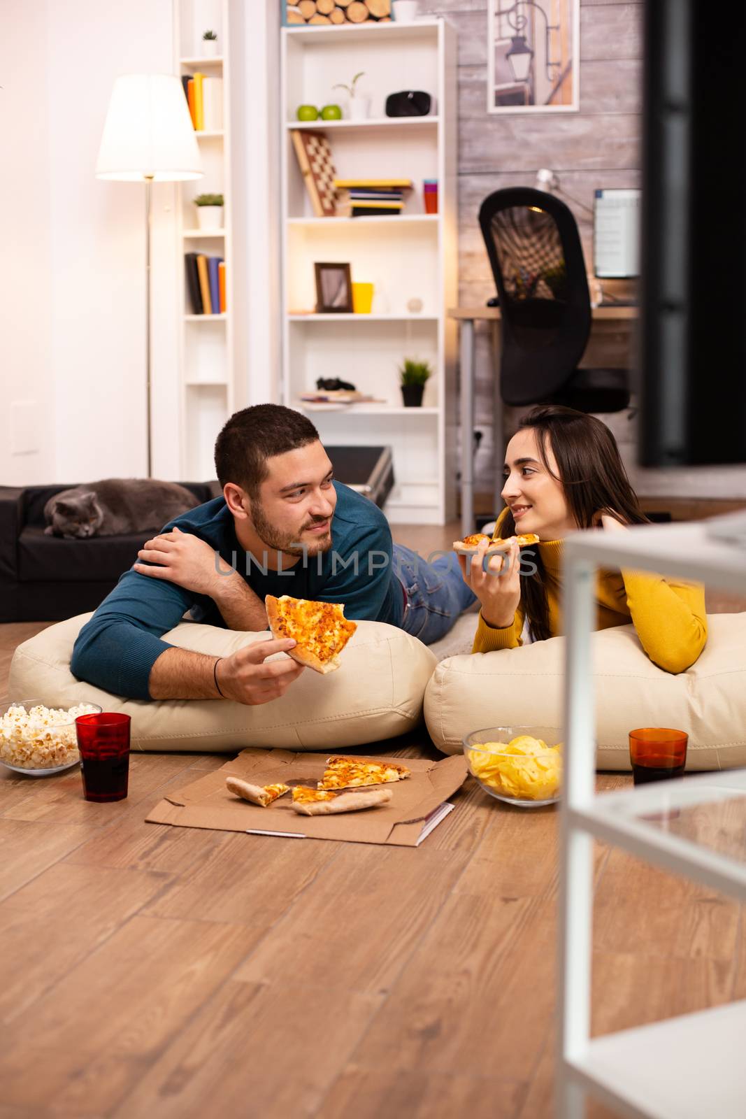 Couple sitting on the floor and watching TV in their living room by DCStudio