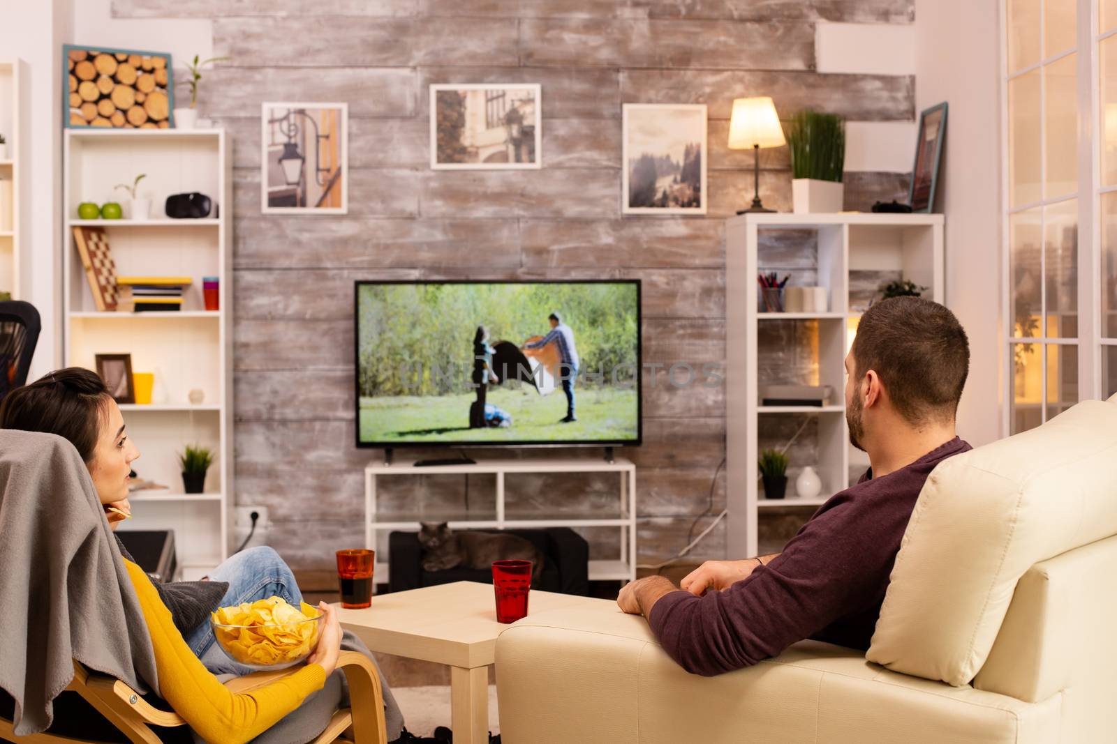 Back view of couple in living room watching a movie on the TV by DCStudio