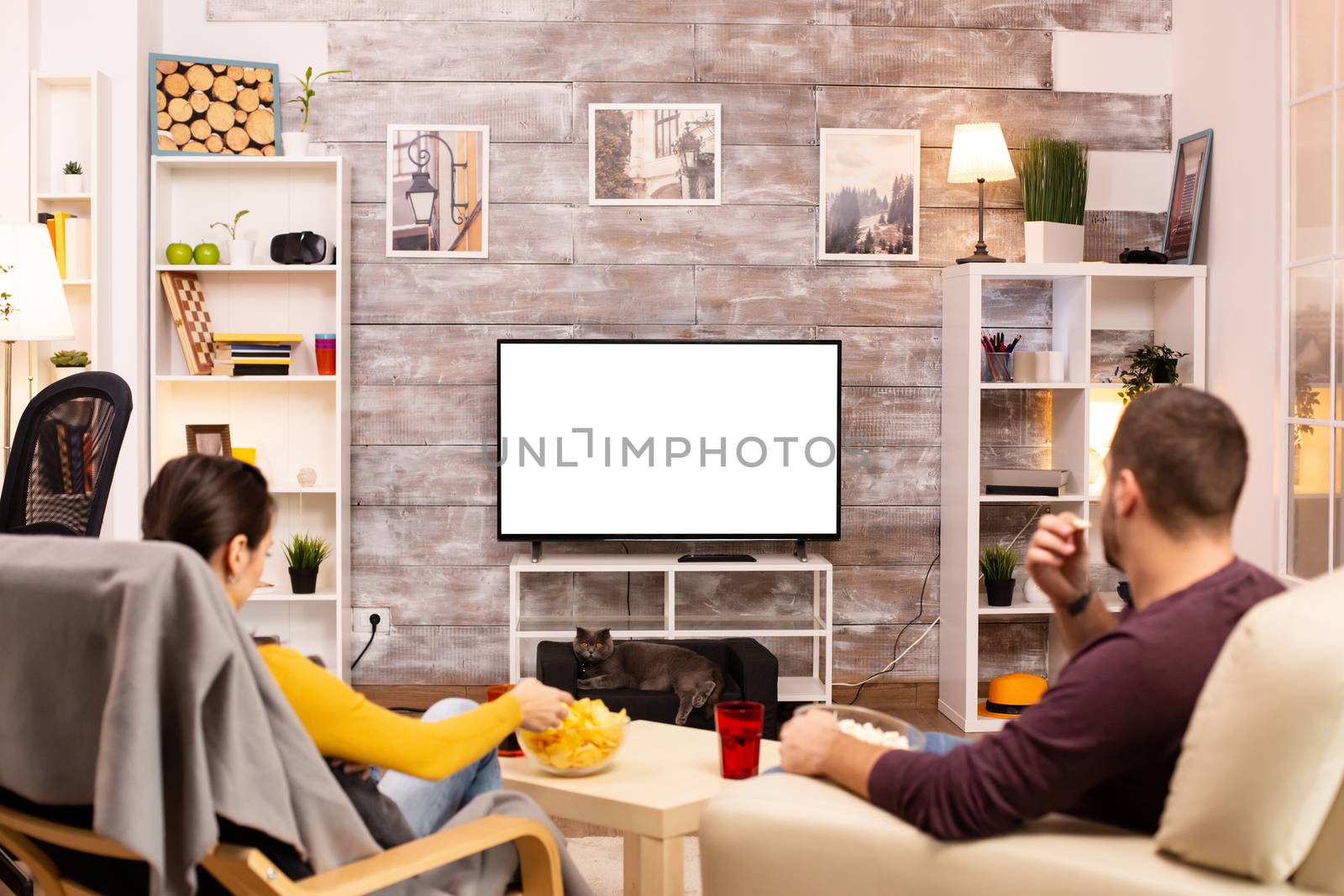 Couple looking at isolated TV screen in cozy living room while eating takeaway food