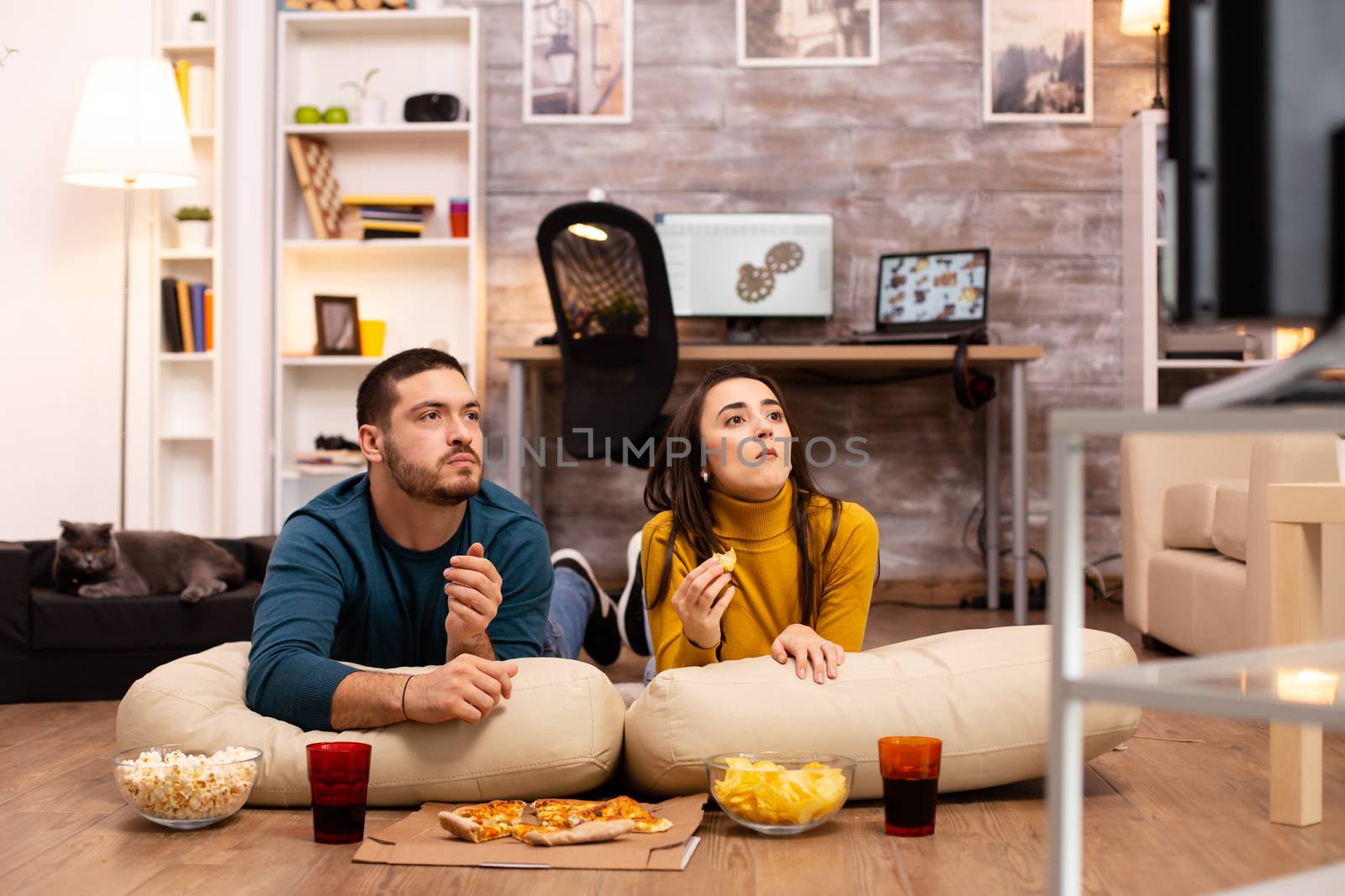 Couple sitting on the floor and watching TV in their living room.