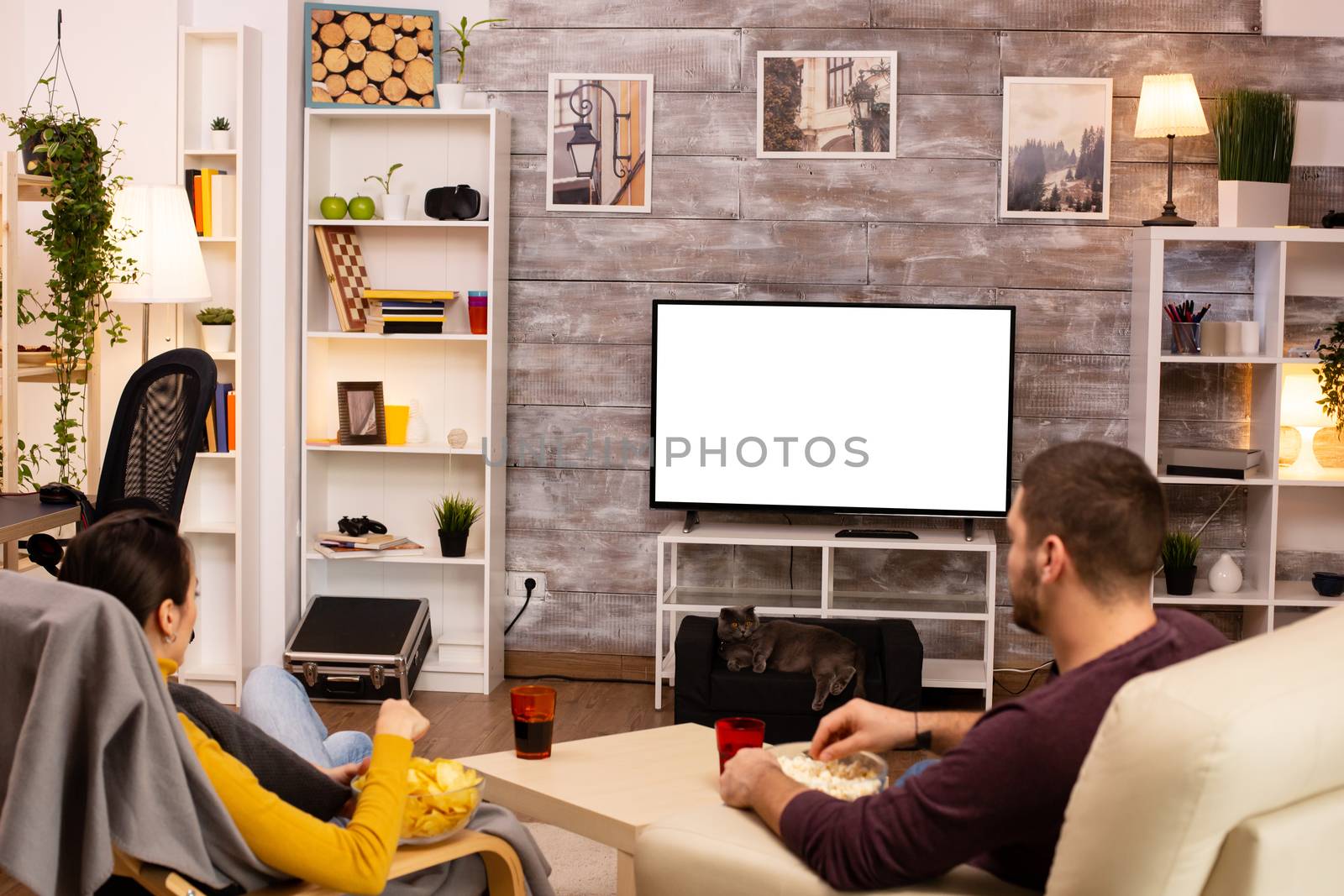 Couple looking at isolated TV screen in cozy living room while eating takeaway food