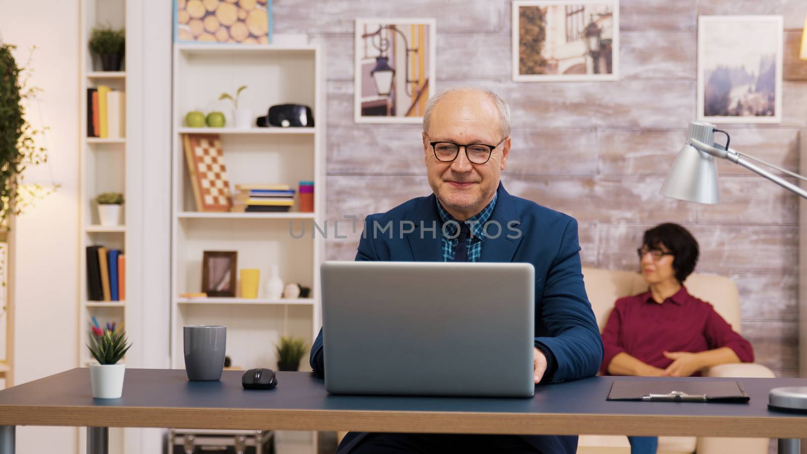 Handsome old man putting on his glasses while working on laptop by DCStudio