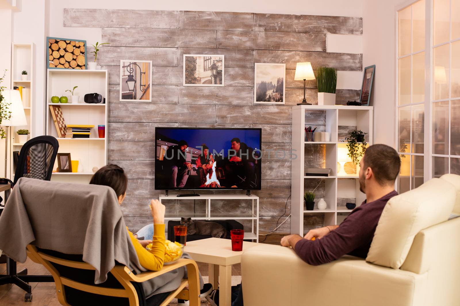 Back view of couple in living room watching a movie on the TV while eating takeaway food