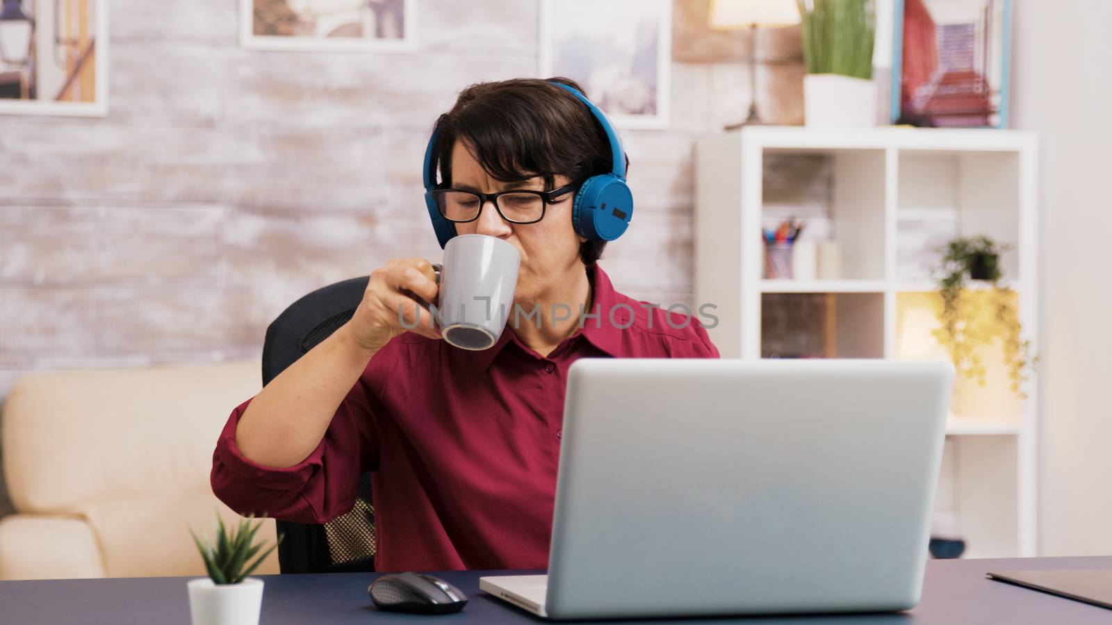 Old woman enjoying a cup of coffee while working on laptop by DCStudio
