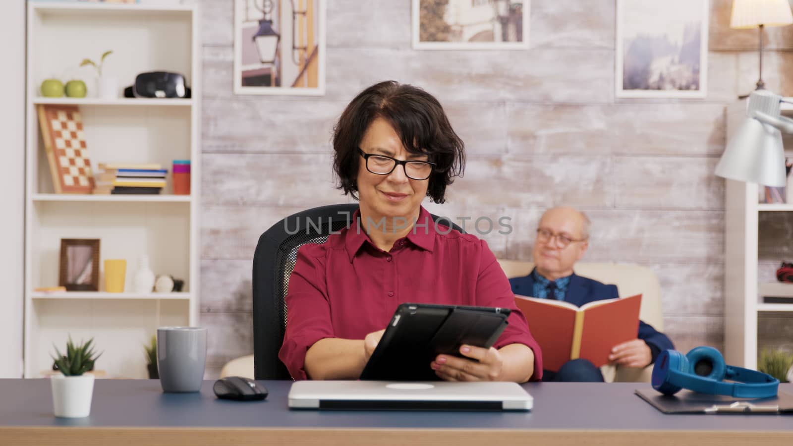 Elderly woman with glasses using tablet in living room by DCStudio