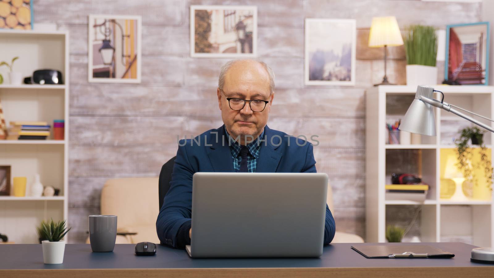 Handsome old man taking a sip of coffee while working on laptop by DCStudio