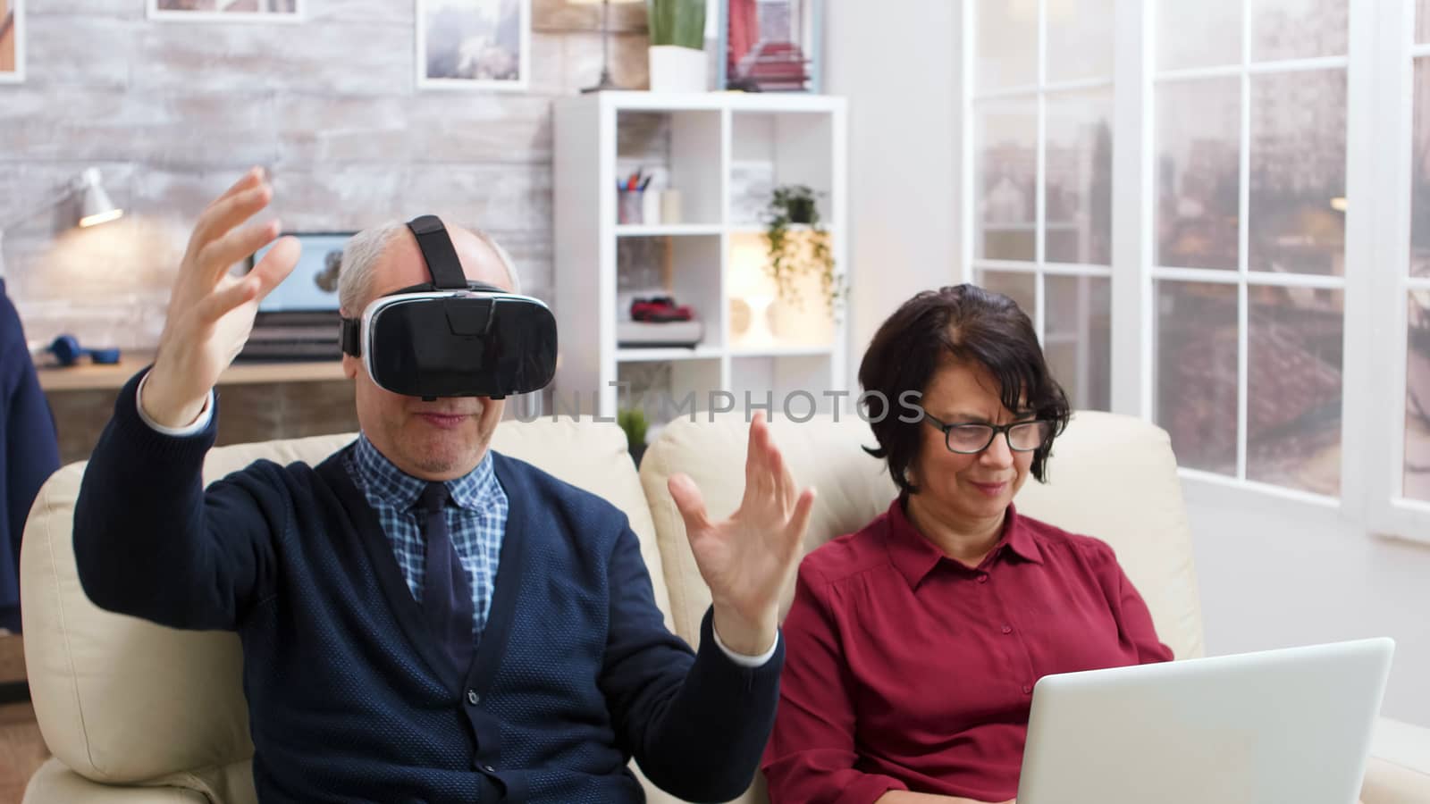 Elderly couple using modern technology to watch movies. Senior with virtual reality goggles. Old lady with laptop.
