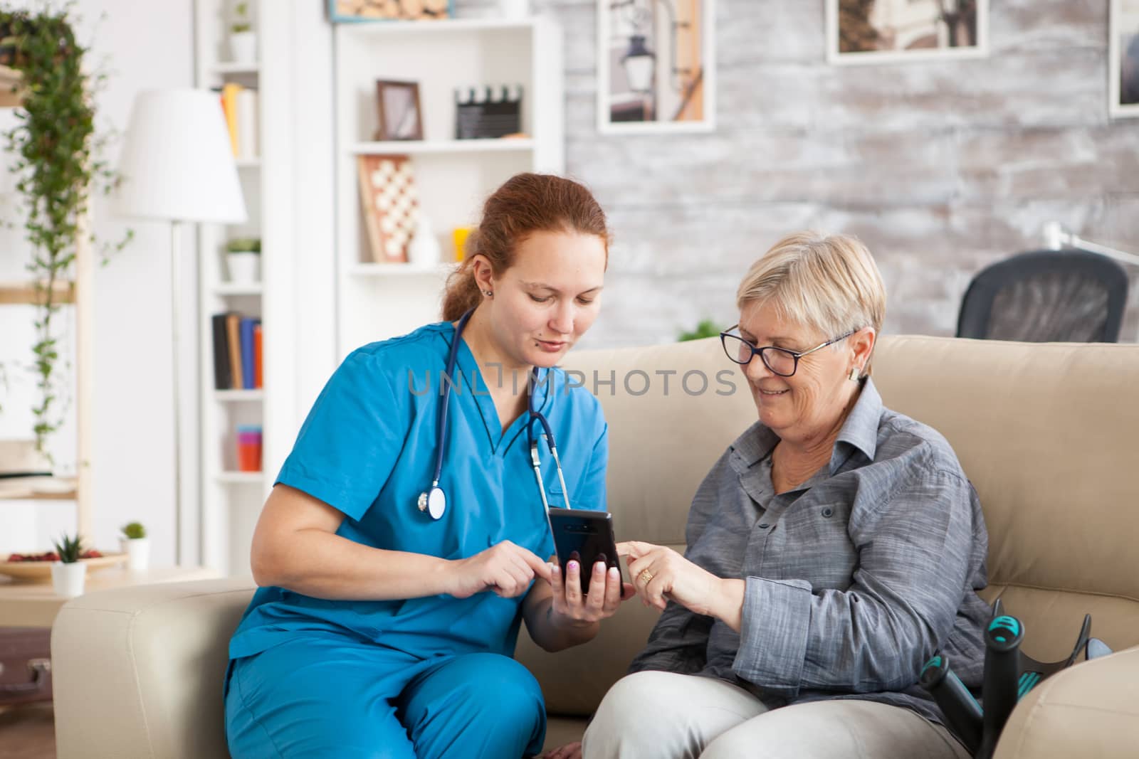 Pretty nurse helping senior woman how to use mobile phone in nursing home.