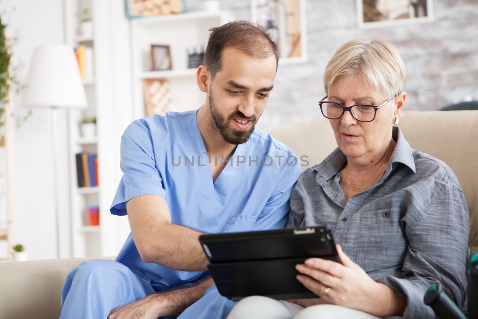 Health visitor helping senior woman to use tablet in nursing home.
