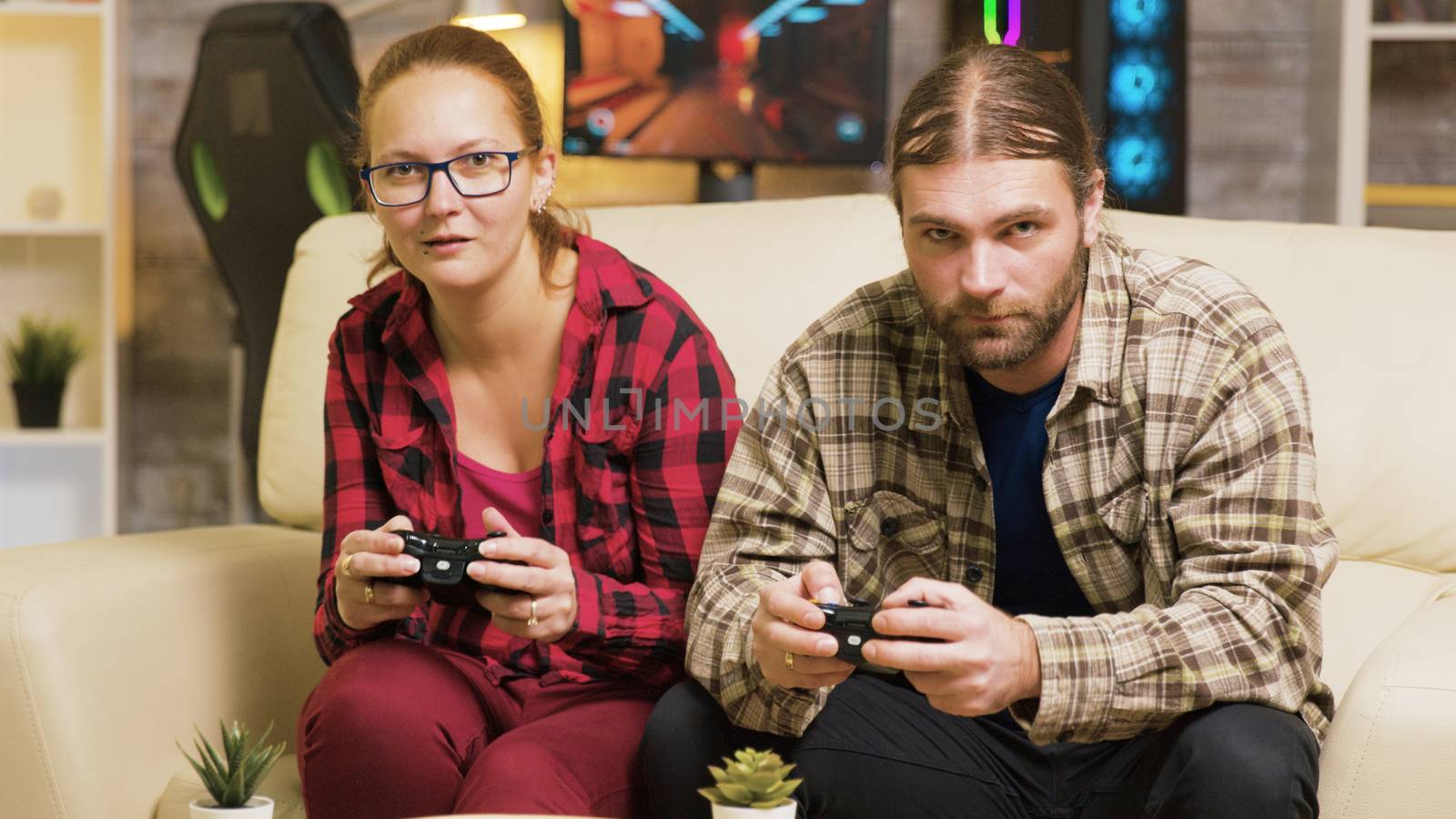 Focused couple playing online video games sitting on couch in living room. Playing games using wireless controllers.