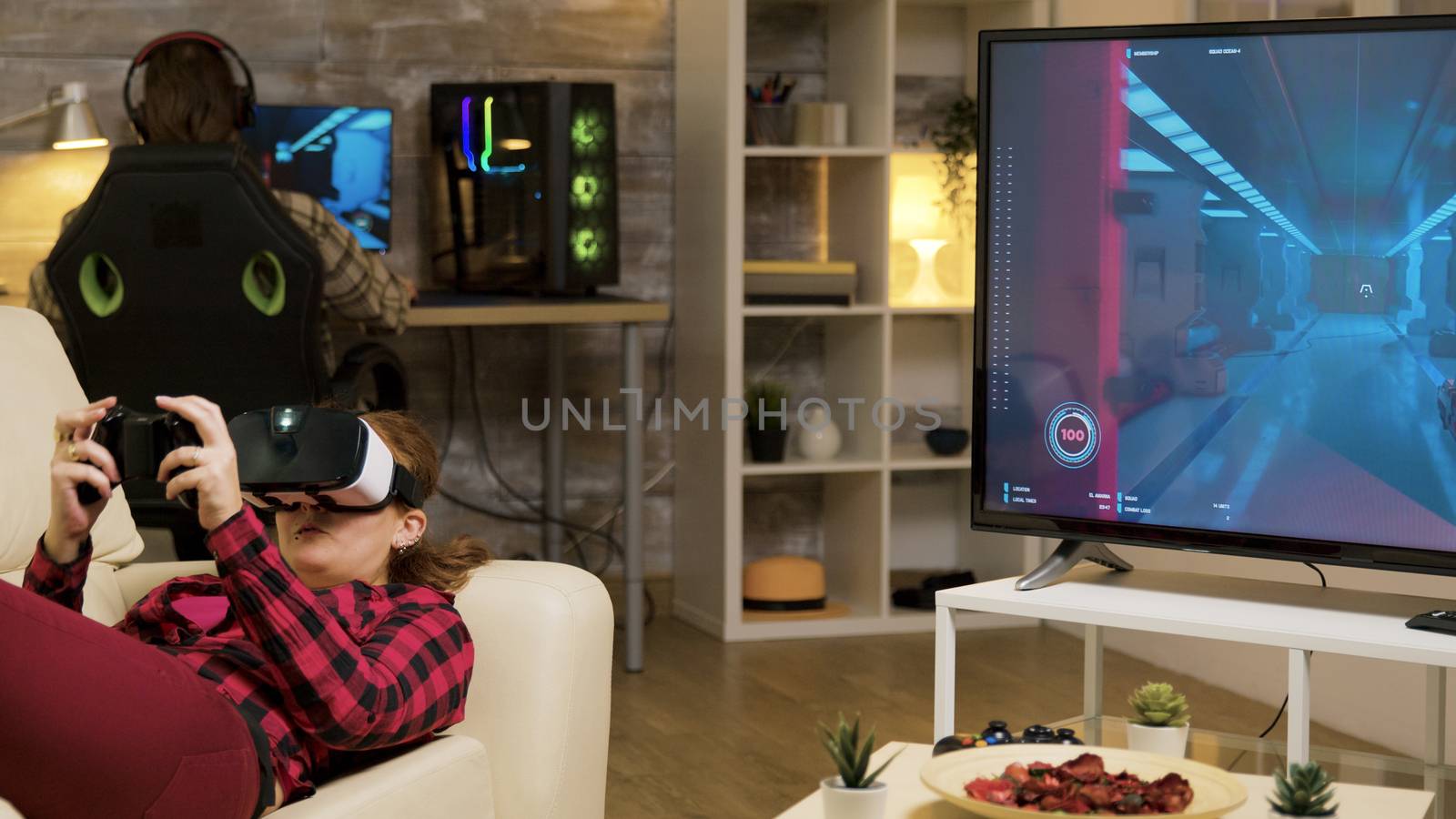 Woman using vr headset to play video games and wireless controller lying on sofa.