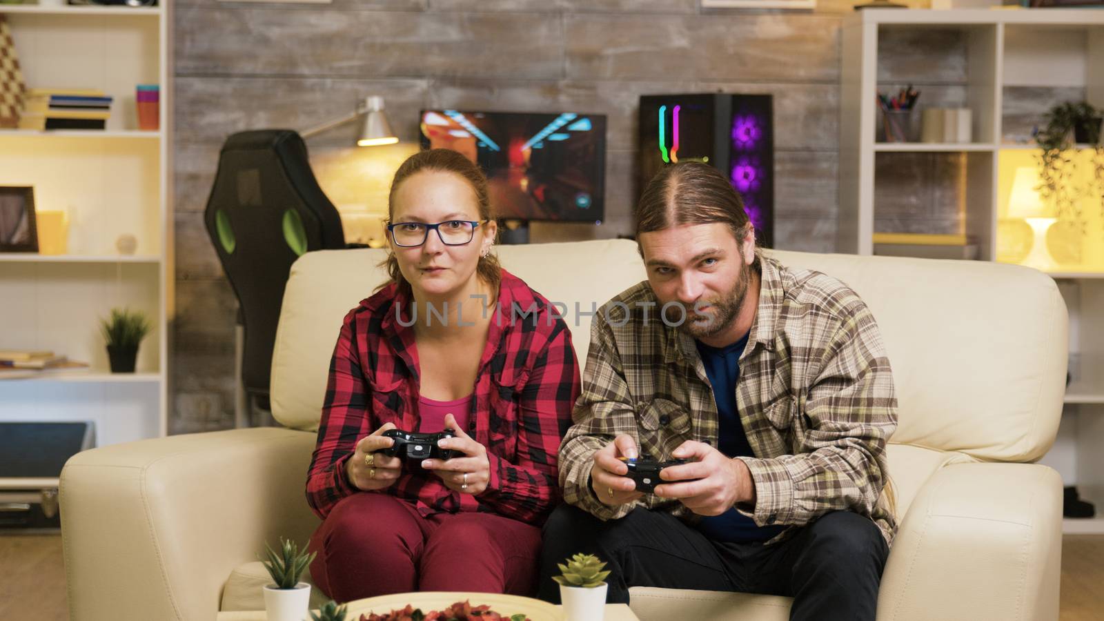 Excited couple giving high five while playing online video games sitting on couch using wireless controllers.