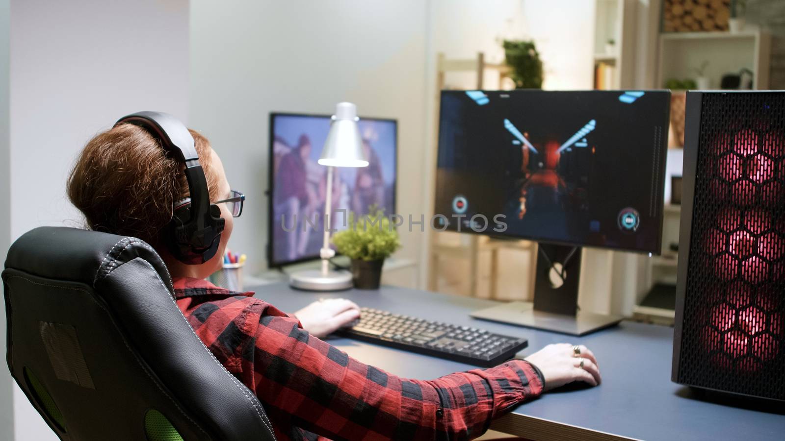 Side view of young female playing shooter games sitting on gaming chair. Powerful computer rig with neon spinning fans