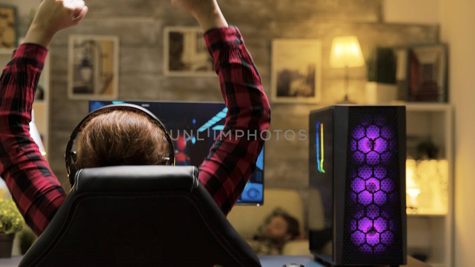 Back view of woman winning at video games while playing late at night. She has a powerful PC with neon fans in the front