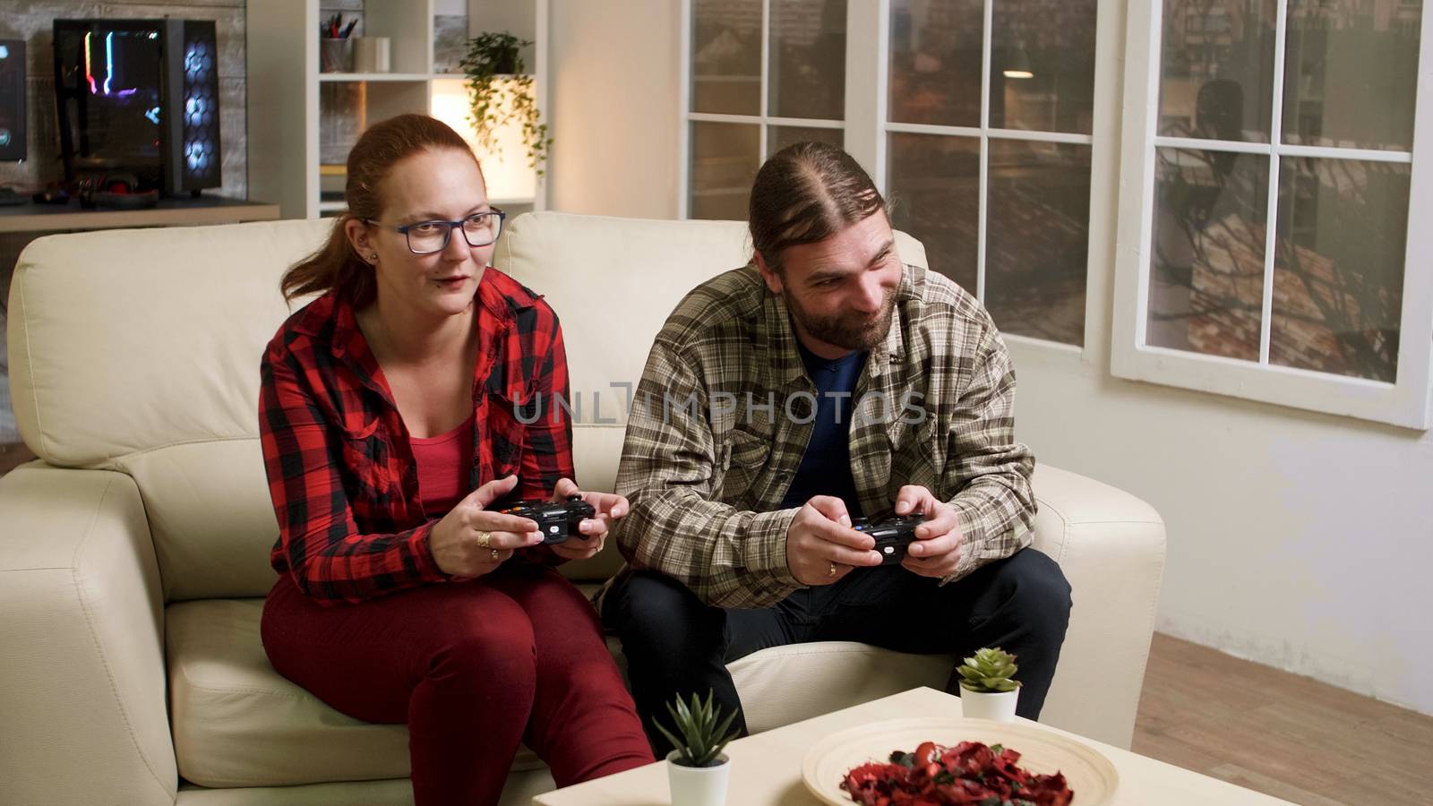 Man and woman sitting on sofa playing video games using wireless joysticks.