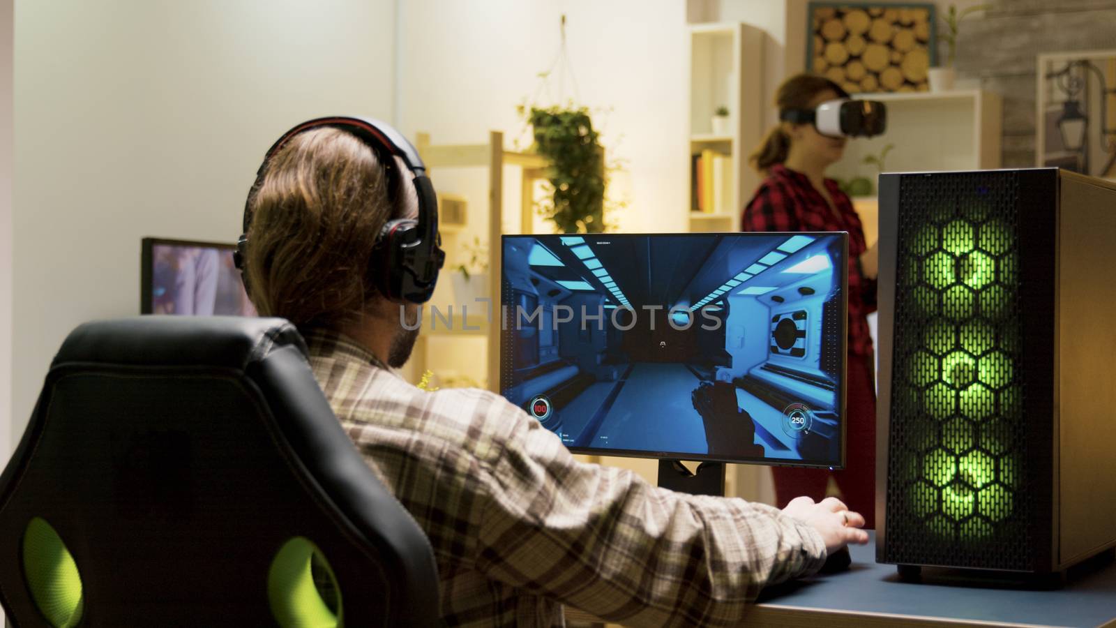 Man putting headphones on and start playing video games on computer. Woman experiencing virtual reality with vr headset in the background.