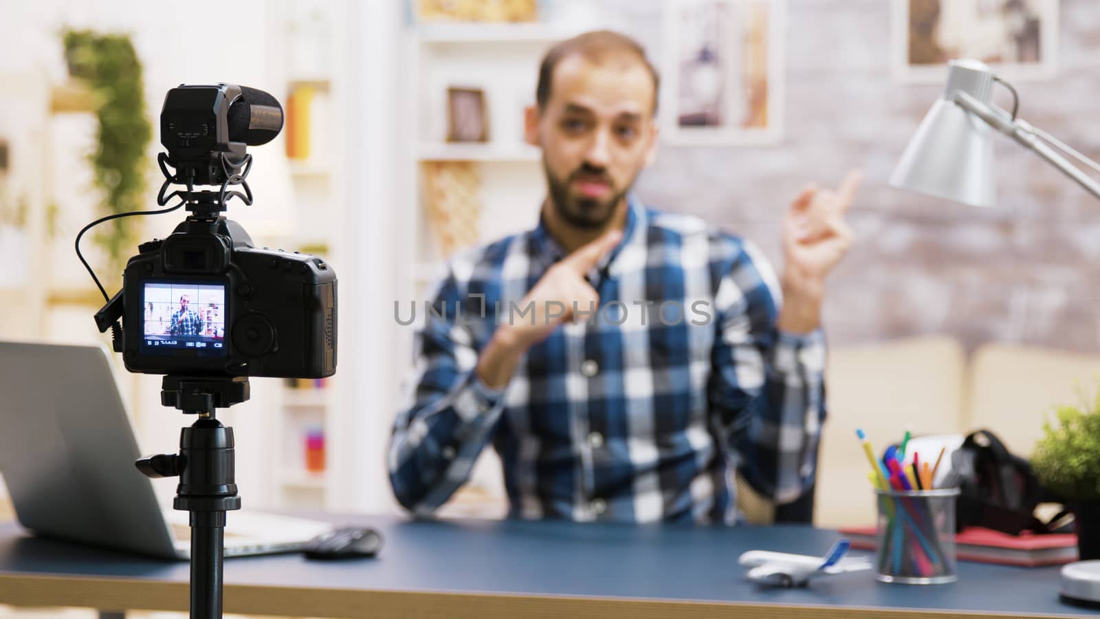 Vlogger sitting at desk in living room talking and looking at the camera by DCStudio