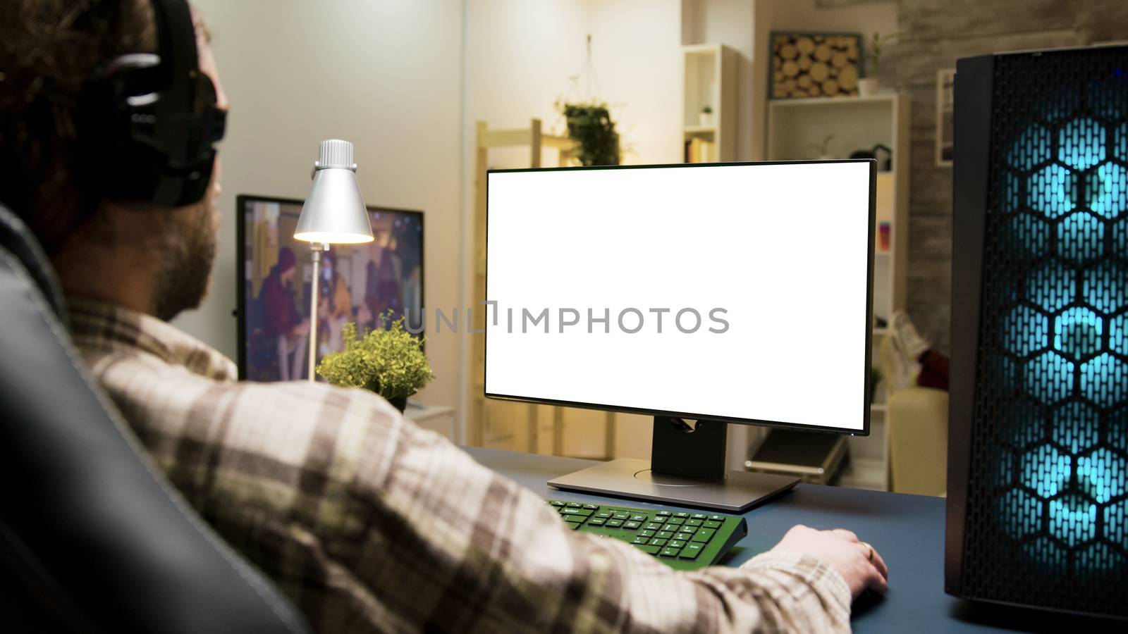 Man with headphones playing games on computer with green screen in living room.