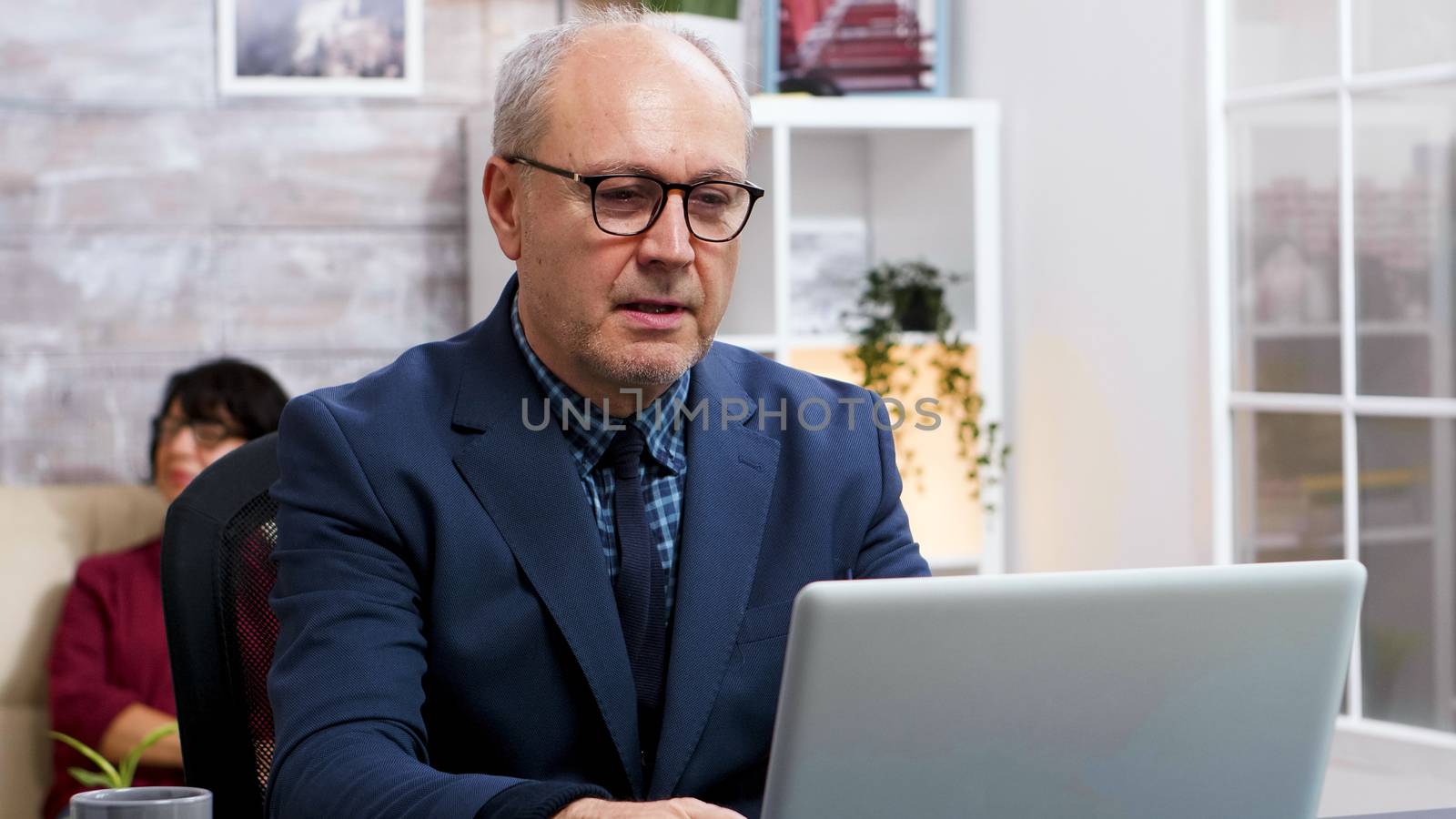 Old man with glasses working on laptop in living room by DCStudio