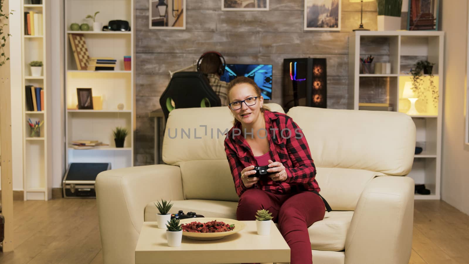 Young woman excited after her victory while playing video games in living room using wireless controller. Boyfriend in the background.