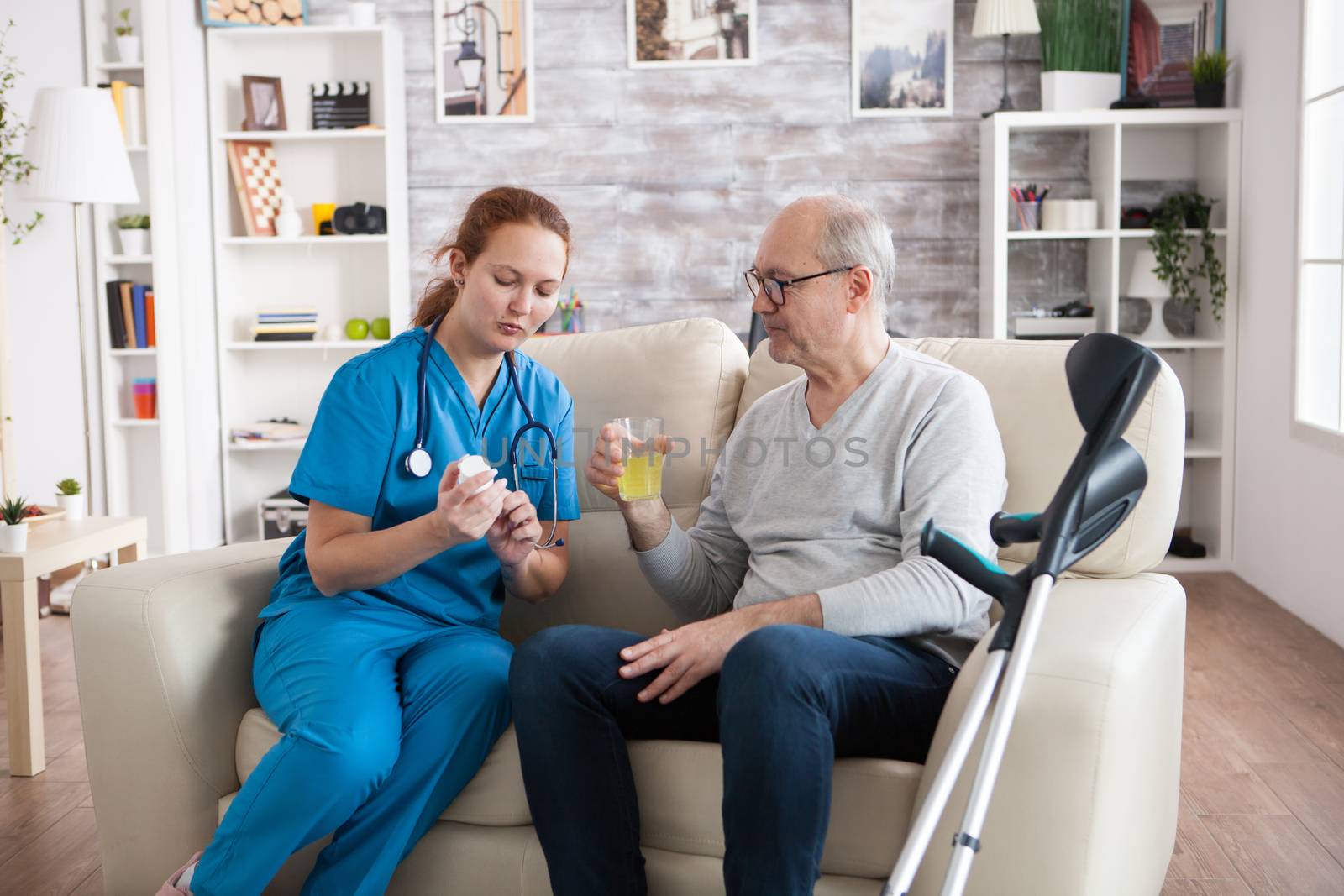 Lady caregiver giving senior man with crutches pills for his disease by DCStudio