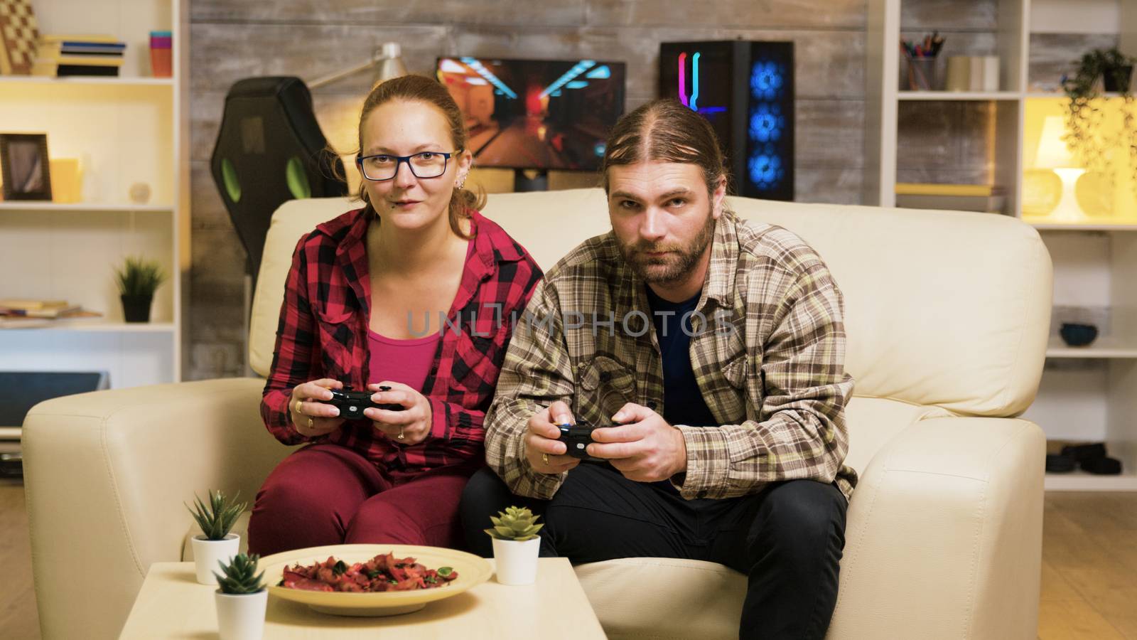 Zoom in shot of beautiful young couple playing video games sitting on couch using controllers.