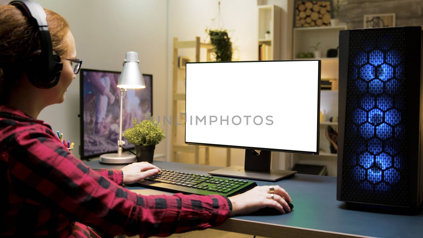 Woman with headphones playing games on green screen computer in living room. Woman sitting on gaming chair.