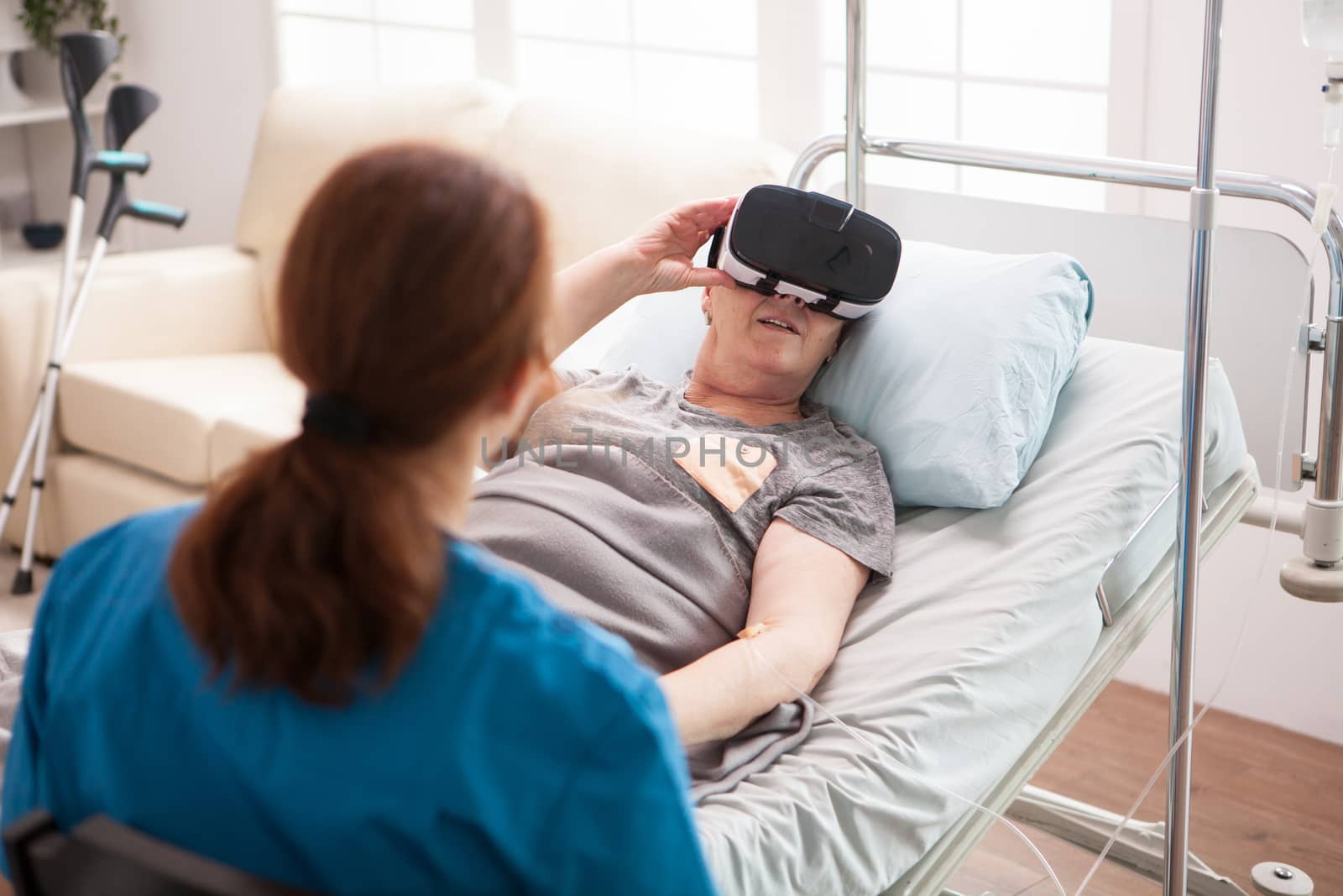 Back view of old woman in nursing home using virtual reality glasses.